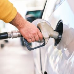 Close-up of a person refueling a car with a gas nozzle at a station.