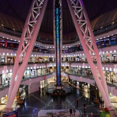A vibrant and spacious modern shopping mall with various shops and people bustling around.