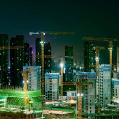 Night view of a bustling construction site in an urban cityscape with cranes and high-rise buildings.