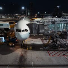 Airplane parked at airport gate during nighttime, unloading cargo and passengers.
