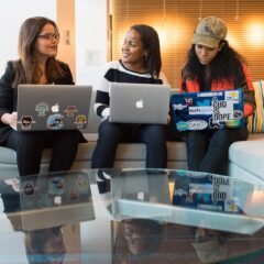 Three women engaging in work discussion with laptops in a modern office environment.