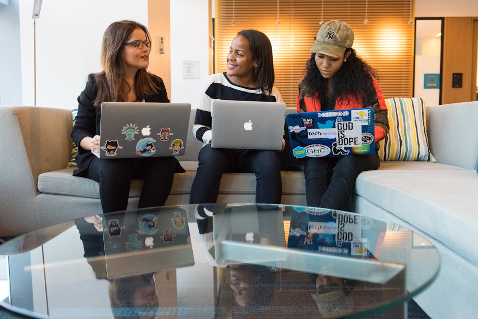 Three women engaging in work discussion with laptops in a modern office environment.