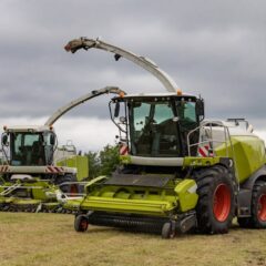 Two modern combine harvesters parked on a farm field under cloudy skies.