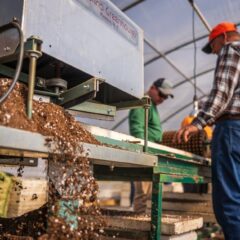 Workers operating machinery in a greenhouse for soil production.