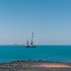 A serene view of offshore wind turbines against a clear blue sky with calm ocean waters.