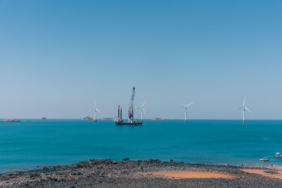 A serene view of offshore wind turbines against a clear blue sky with calm ocean waters.