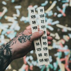 Close-up of a tattooed hand holding raffle tickets amidst confetti at a festival setting.