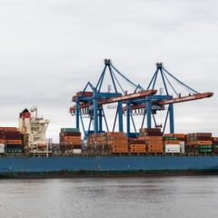 A container ship docked at Hamburg port surrounded by cranes and shipping containers.
