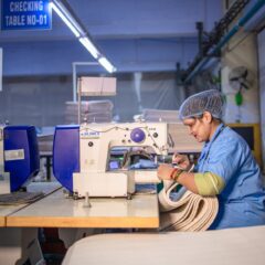 A woman operating a sewing machine in a textile factory, focused and skilled.