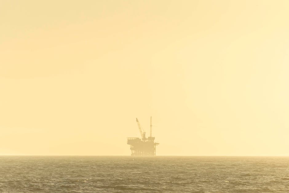 Distant view of an offshore oil platform against a golden sky at sunset over a calm sea.