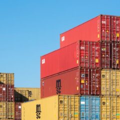 A vibrant collection of stacked shipping containers under a clear, blue sky. Ideal for logistic themes.