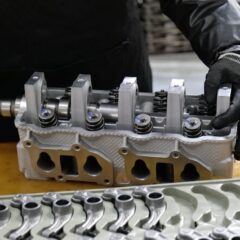 Mechanic assembling an engine cylinder head with precision components on a workbench.