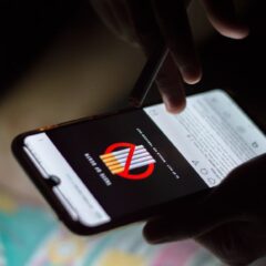 A person browsing social media on a smartphone at night, holding a cigarette.