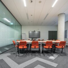 Spacious conference room with a large meeting table, red chairs, and glass walls for natural lighting.
