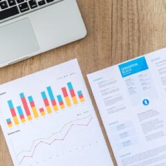 Top view of a laptop, charts, and resume on a wooden desk, showcasing business analysis and job application.