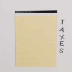 Close-up of a yellow legal pad and the word 'TAXES' on a white surface, ideal for finance themes.