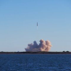 A rocket launch with smoke trails over South Padre Island, viewed across the ocean.