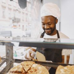 A cheerful baker in an apron serves pastries in a bright bakery display.