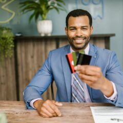 Smiling African American man in a suit holding credit cards at a business desk.