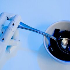 A robotic hand holding a spoon above a bowl with keyboard keys, showcasing technology themes.
