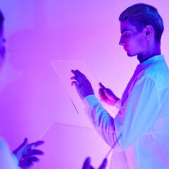 Two individuals engaging with futuristic transparent touch screens in a vibrant purple-lit studio.