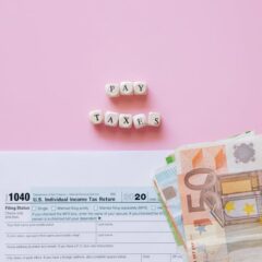 Top view of tax form, euro banknotes, and 'Pay Taxes' letter blocks on pink background.