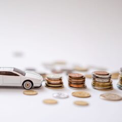 White toy sports car beside stacks of coins on a white background, emphasizing savings and finance.