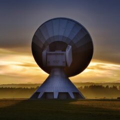 Large satellite dish silhouette against a colorful sunset, showcasing broadcasting technology.