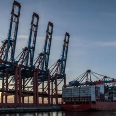 Container cranes and a cargo ship at Hamburg port during sunset, showcasing industrial logistics.