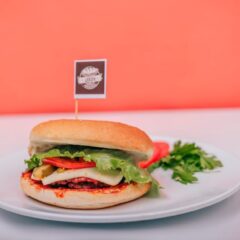 A vegetarian burger with lettuce, cheese, and tomato on a plate against a vibrant background.