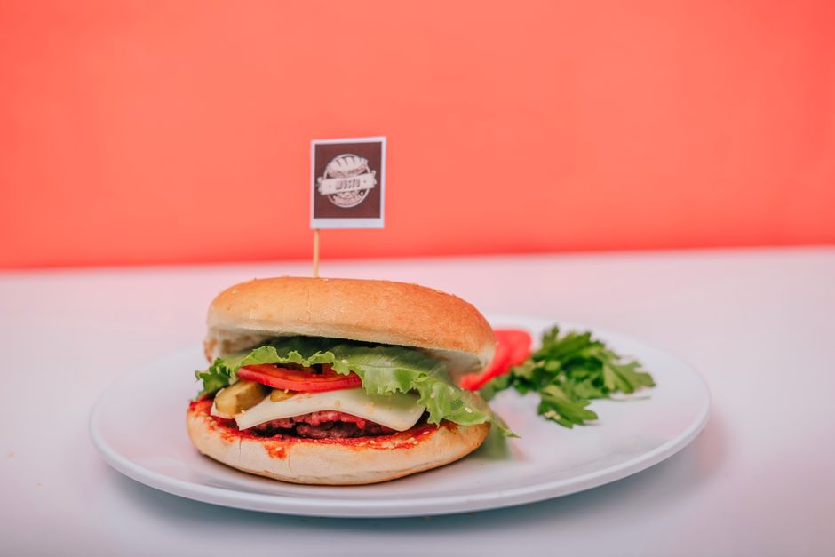 A vegetarian burger with lettuce, cheese, and tomato on a plate against a vibrant background.