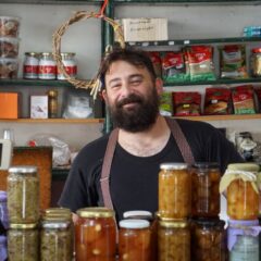 A friendly shopkeeper stands behind shelves of homemade preserves.