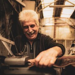 Elderly man joyfully crafting in his rustic workshop with natural light.
