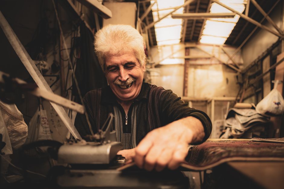 Elderly man joyfully crafting in his rustic workshop with natural light.