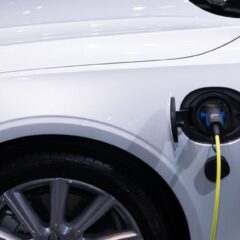 A white electric car is plugged in for charging, close-up view of the charging port.