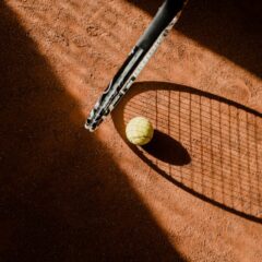 Tennis ball with racket shadow on a sunlit clay court.