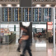 Blurred motion of travelers in a modern airport terminal with departure screens and a prominent clock.