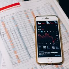 Smartphone displaying stock market data on papers with financial charts.