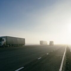 Freight trucks on a foggy road during sunrise, showcasing transportation in misty conditions.