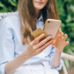 A woman making an online purchase using a smartphone and credit card outdoors.