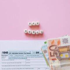 Top view of tax form, euro banknotes, and 'Pay Taxes' letter blocks on pink background.