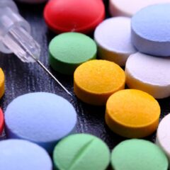 Vibrant close-up of assorted pills and a syringe needle.