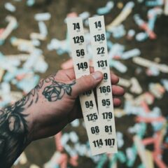 Close-up of a tattooed hand holding raffle tickets amidst confetti at a festival setting.