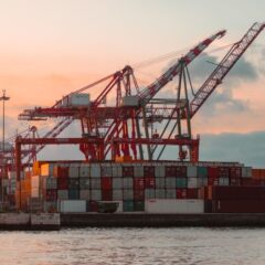 Container cranes at a bustling port during sunset, creating a vibrant industrial scene.