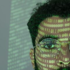 Close-up of a man with binary code projected on his face, symbolizing cybersecurity.