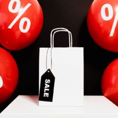 White shopping bag with sale tag surrounded by red balloons displaying percentage signs.