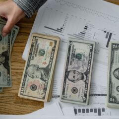 Person holds US dollars over financial papers, showing income or budget analysis.