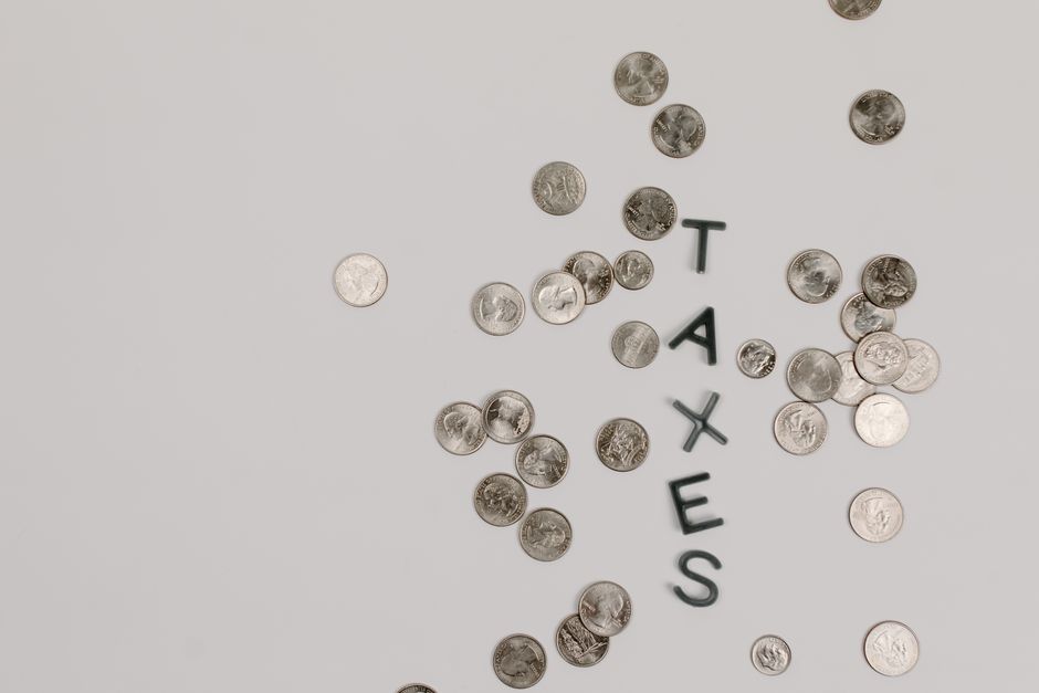 Scattered coins forming the word 'TAXES' on a white surface, symbolizing financial concepts.