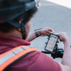 A delivery rider checks directions on a smartphone mounted on a scooter outdoors.