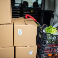 Cardboard boxes and fresh produce being prepared for delivery in a van, highlighting logistics and farm-to-table movement.